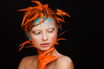 Portrait of a beautiful model with creative make-up and hairstyle using orange feathers