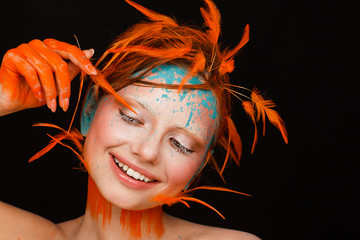 Portrait of a beautiful model with creative make-up and hairstyle using orange feathers