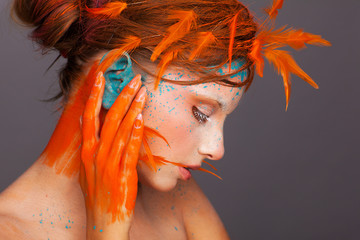 Portrait of a beautiful model with creative make-up and hairstyle using orange feathers