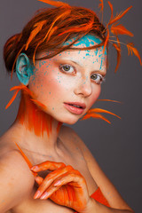 Portrait of a beautiful model with creative make-up and hairstyle using orange feathers