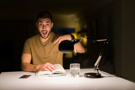 Young handsome student man studying at night at home with surprise face pointing finger to himself