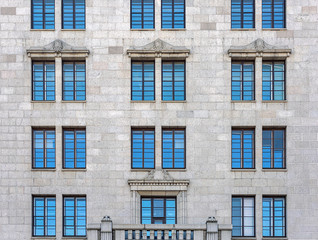 The facade of the city building faced with gray stone. The Windows reflect the blue sky