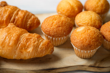 Close-up of cupcakes and croissants prepared for breakfast on wooden board on white wooden table.