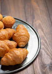 Close-up of cupcakes and croissants on metal tray on brown wooden table. Vertical shoot.