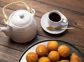 Cupcakes and croissants on metal tray with coffee cup and coffee maker. Breakfast.