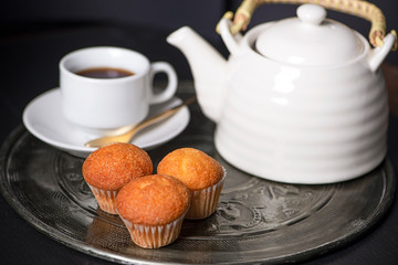 Cupcakes next to cup of coffee maker on metal tray.