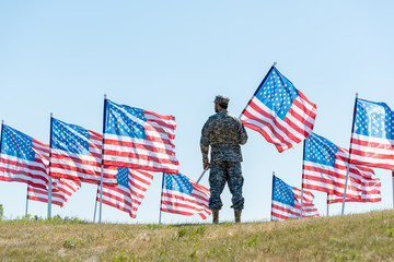 selective focus of soldier in military uniform and cap standing and holding american flag