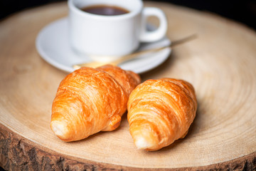 Close-up of two croissants next to cup of coffee on wooden board.