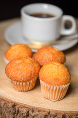 Vertical shoot of several cupcakes next to cup of coffee on wooden board. Sweets for breakfast.