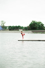 Fototapeta premium Asian young girl doing yoga outdoors on the pier by the lake.