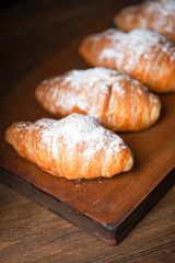 Vertical shoot of several croissants with sugar on top over wooden board. Sweet for breakfast.