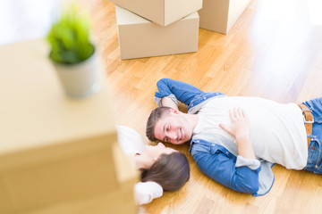 Young beautiful couple relaxing lying on the floor around cardboard boxes at home, smiling happy moving to a new house