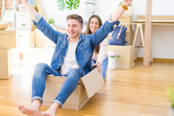 Beautiful young couple smiling in love having fun riding inside a cardboard box, celebrating moving to a new home