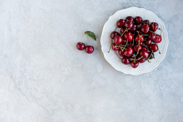 Raw cherries in plate on gray background