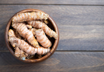 From above turmeric roots in a wooden bowl on brown wooden table. Specia for health and cooking ingredient. Copy space.