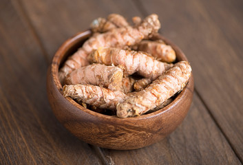 Turmeric roots in a wooden bowl on brown wooden table. Specia for health and cooking ingredient.