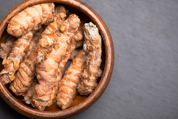 Bowl with turmeric root on black slate base with copy space on the right. Spice for health and ingredient of Indian cuisine.