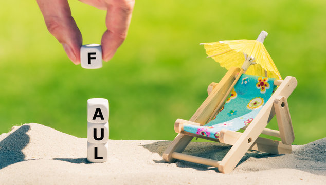 Am Sandstrand bilden W&uuml;rfeln das Wort "Faul" neben einer kleinen Sonnen-liege und einem Sonnenschirm.