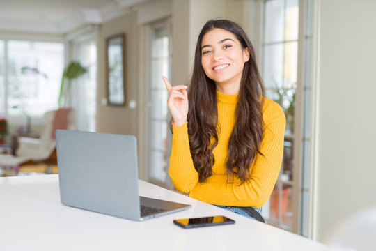 Young woman using computer laptop with a big smile on face, pointing with hand and finger to the side looking at the camera.