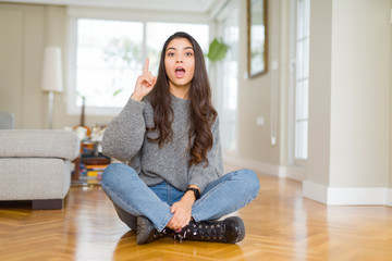 Young beautiful woman sitting on the floor at home pointing finger up with successful idea. Exited...