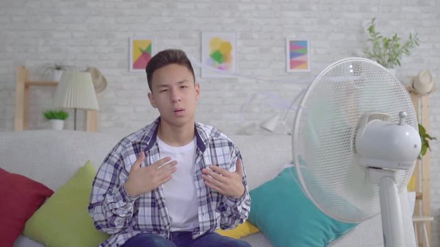 Young asian man saved from the heat sitting in front of a working fan the concept of heat slow mo