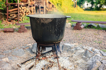 Outdoor country side cuisine with cauldron metal pot kettle for cooking outdoor in the middle of the nature near the camp with the campfire, cooking at the camp fire traditional dish.