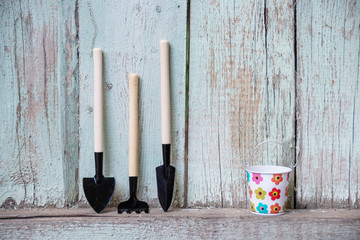 A set of shovels and a rake on a wooden fence with a small empty bucket