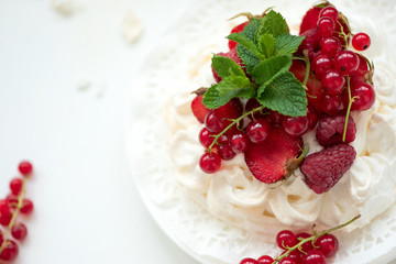 Pavlova fruit cake with strawberry, raspberry, red currant and mint leaves on white background. Selective focus. Healthy food concept