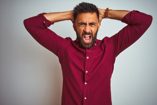 Young indian man wearing red elegant shirt standing over isolated grey background Crazy and scared with hands on head, afraid and surprised of shock with open mouth