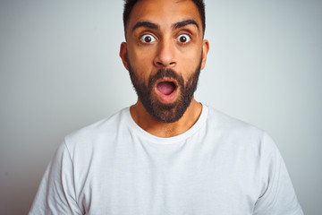 Young indian man wearing t-shirt standing over isolated white background afraid and shocked with surprise expression, fear and excited face.