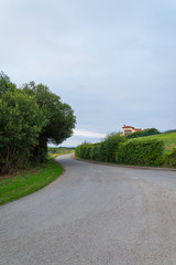 Local road with house, meadows and trees, a cloudy afternoon at sunset in Cantabria, Spain, Europe