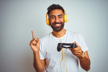 Arab indian gamer man playing video game using headphones over isolated white background very happy pointing with hand and finger to the side - obrazy, fototapety, plakaty