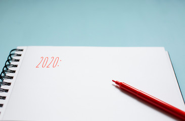 Red pen on a blank white notebook with old wooden background. New Year 2020