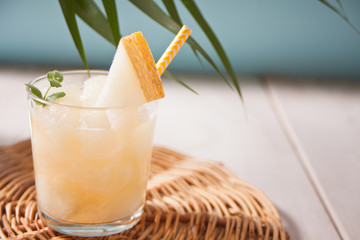 Glass with melon cocktail on a white tablewith the palm leaf in tropical theme