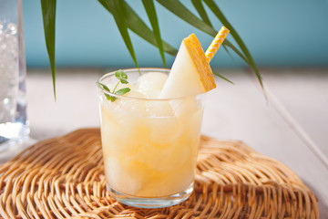 Glass with melon cocktail on a white tablewith the palm leaf in tropical theme