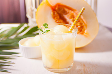 Glass with melon cocktail on a white tablewith the palm leaf in tropical theme