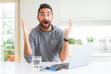 Handsome hispanic man working using computer laptop celebrating crazy and amazed for success with arms raised and open eyes screaming excited. Winner concept