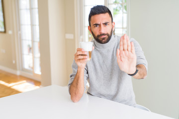 Handsome hispanic man drinking a cup of coffee with open hand doing stop sign with serious and...