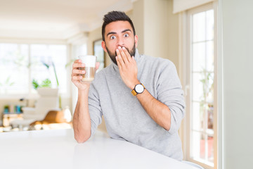 Handsome hispanic man drinking a cup of coffee cover mouth with hand shocked with shame for mistake, expression of fear, scared in silence, secret concept