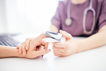 Doctor in purple uniform and shethoskope on a neck holds patient's hand with oximeter at patient's...