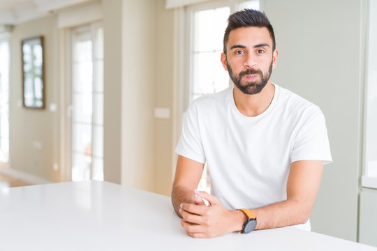 Handsome hispanic man casual white t-shirt at home puffing cheeks with funny face. Mouth inflated with air, crazy expression.
