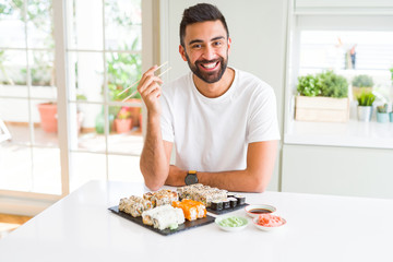Handsome hispanic man eating asian sushi using chopsticks with a happy face standing and smiling with a confident smile showing teeth