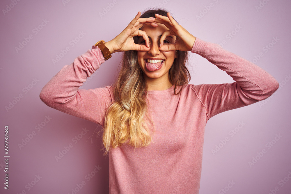 Poster Young beautiful woman wearing a sweater over pink isolated background doing ok gesture like binoculars sticking tongue out, eyes looking through fingers. Crazy expression.