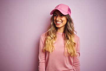 Young beautiful woman wearing cap over pink isolated background looking away to side with smile on face, natural expression. Laughing confident.