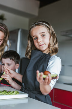 Little girl demonstrating half of ripe avocado to camera while standing in the kitchen looking at camera