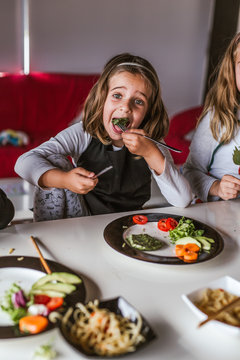 Girl eating vegetarian cutlets and vegetables while sitting at table at home