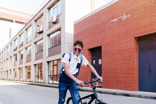 Young smiling black successful man with Afro hair in casual outfit and stylish sunglasses standing with bicycle on street
