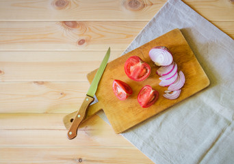 Cutting board, knife and cutted  tomato and purple onion on wooden background.
