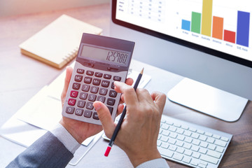 Businessman using calculator reviewing a financial statements and reports for business performance and a return on investment or investment risk analysis.