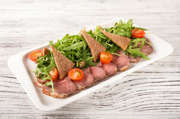 Baked ham with arugula and bread croutons close-up. Snack from jamon, arugula and cherry on a white plate copy space.